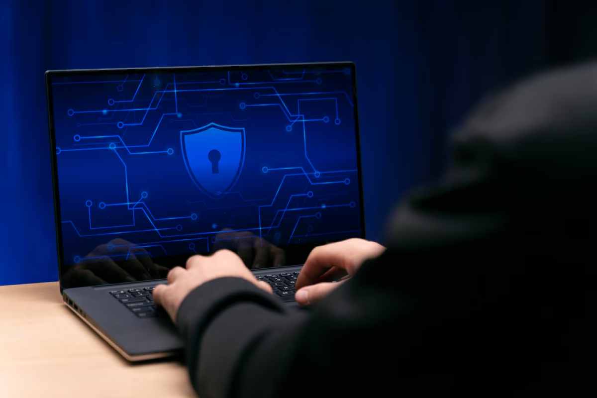 Person using a laptop displaying a cybersecurity lock icon on a blue digital background.