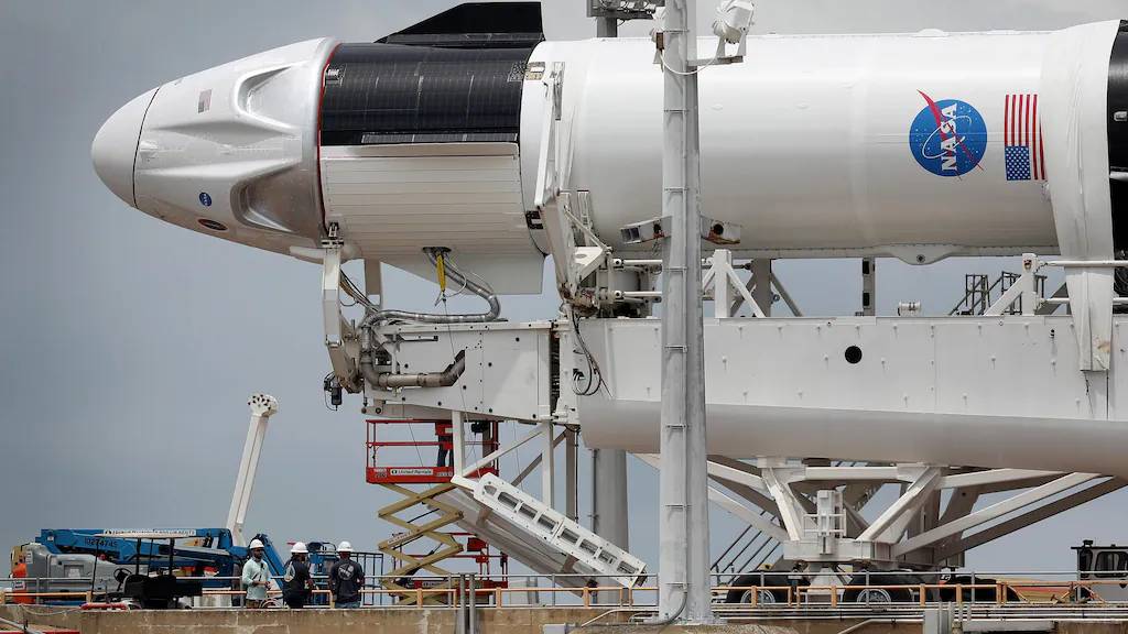 A rocket with crew capsule being prepared by technicians on a launchpad.