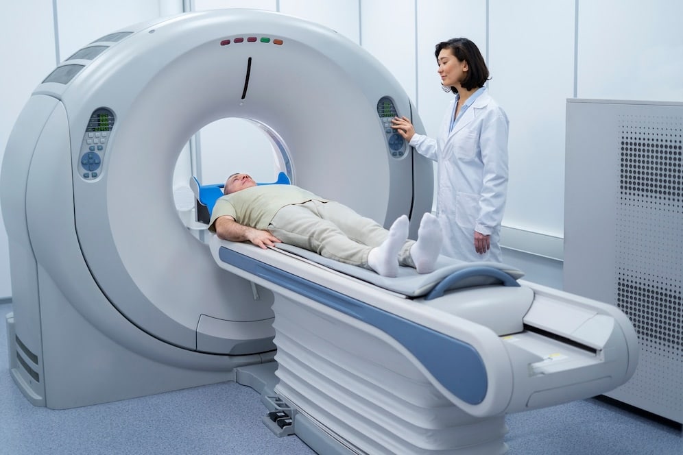 A patient is lying on a CT scan machine while a medical professional operates