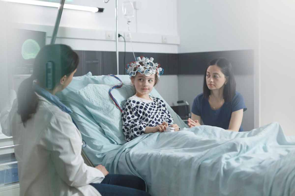 A child wearing an EEG cap sits on a hospital bed