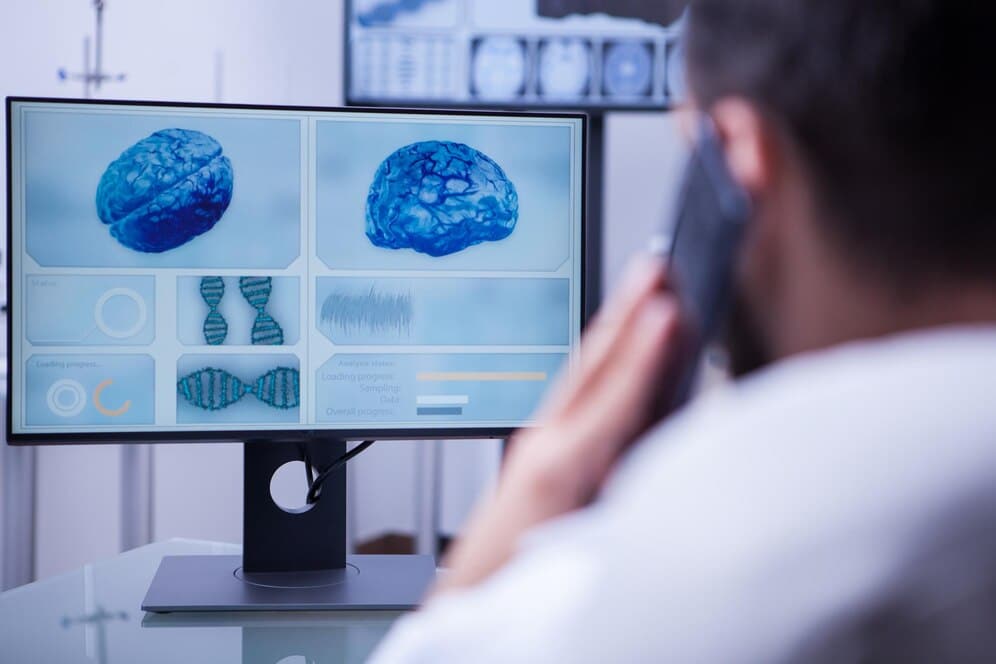 A healthcare professional observes a screen displaying brain and DNA images