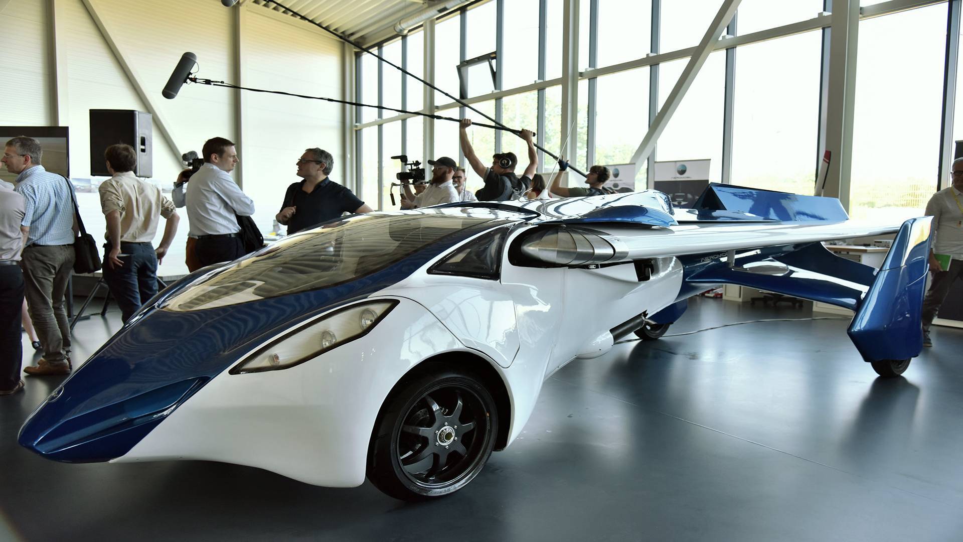 People observing a futuristic white and blue flying car 
