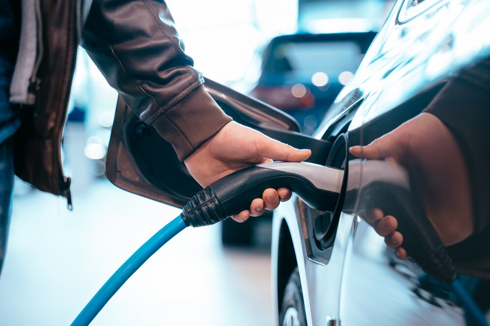 A person charging cable into an electric vehicle at a charging station.