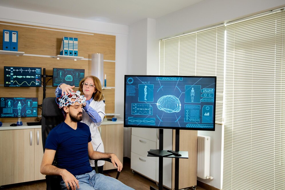 A woman adjusts a high-tech helmet on a seated man in a modern laboratory with digital displays.