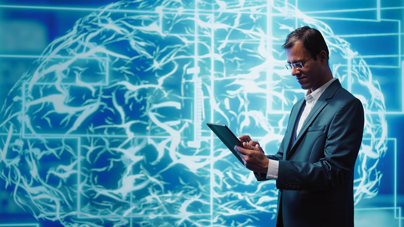 Man in suit examines tablet, standing before a digital brain