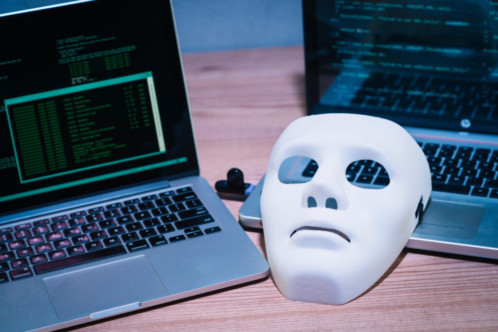 Two laptops displaying code on a desk beside a white mask.