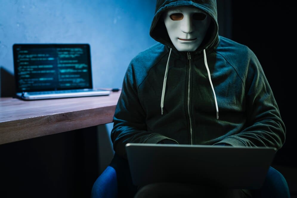 A person in a dark hoodie sits at a desk with a laptop