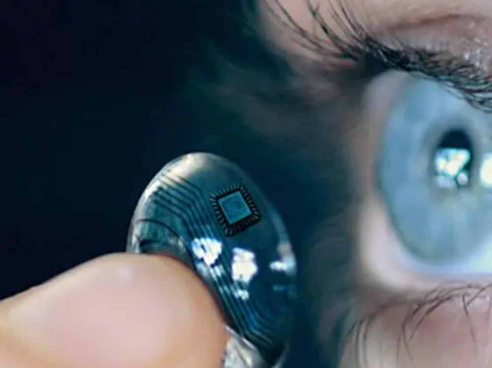 Close-up of a futuristic contact lens with a microchip being held near a human eye.
