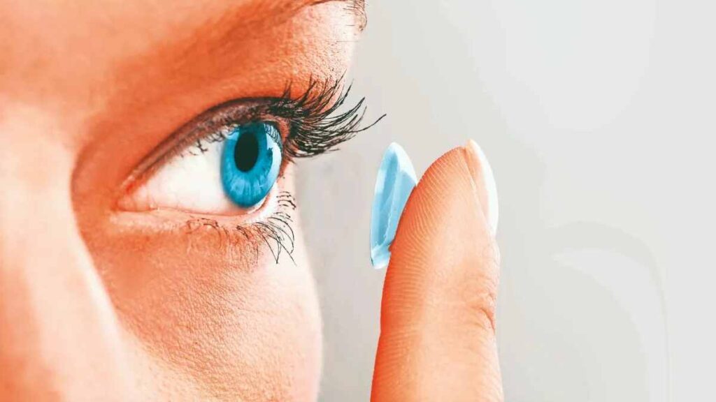 Close-up of a person inserting a blue contact lens into their eye.