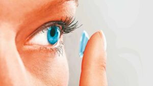 Close-up of a person inserting a blue contact lens into their eye.