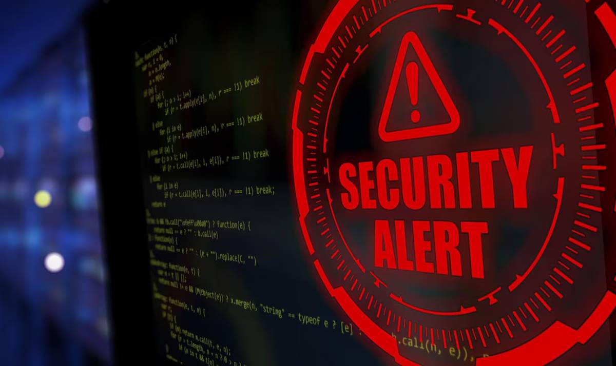 A red SECURITY ALERT warning sign with coding script on a monitor in the background.