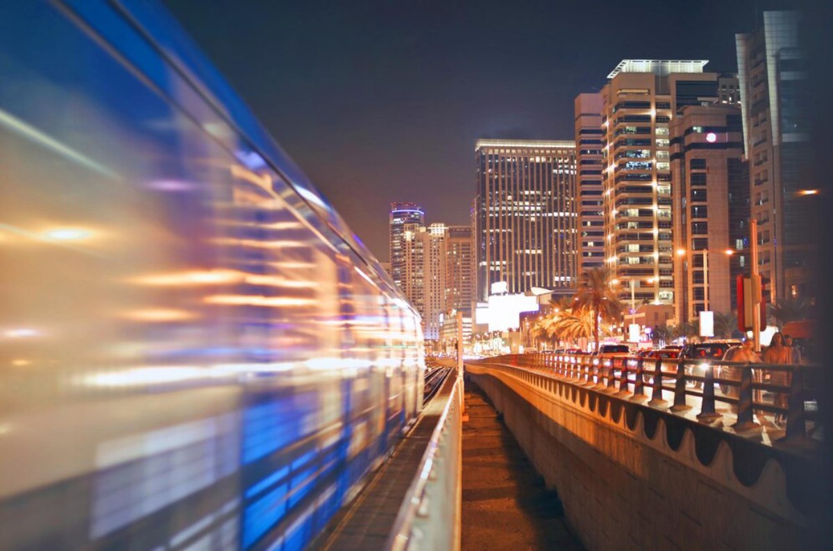 Blurred metro train in motion at night with illuminated city buildings in the background.