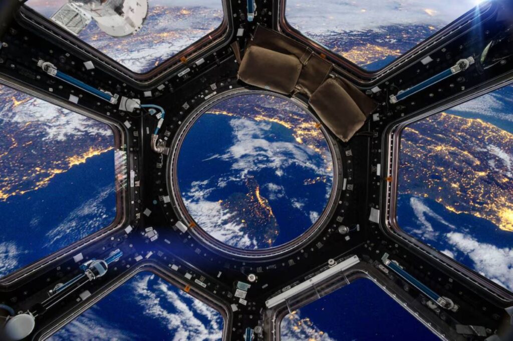 View of Earth from the International Space Station with city lights and clouds visible through a window.
