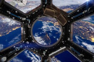 View of Earth from the International Space Station with city lights and clouds visible through a window.